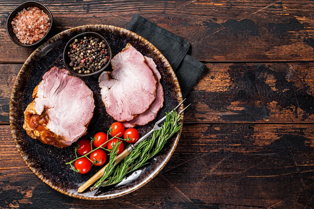 Smoked pork meat - gammon with herbs on rustic plate. Wooden background. Top view. Copy space.