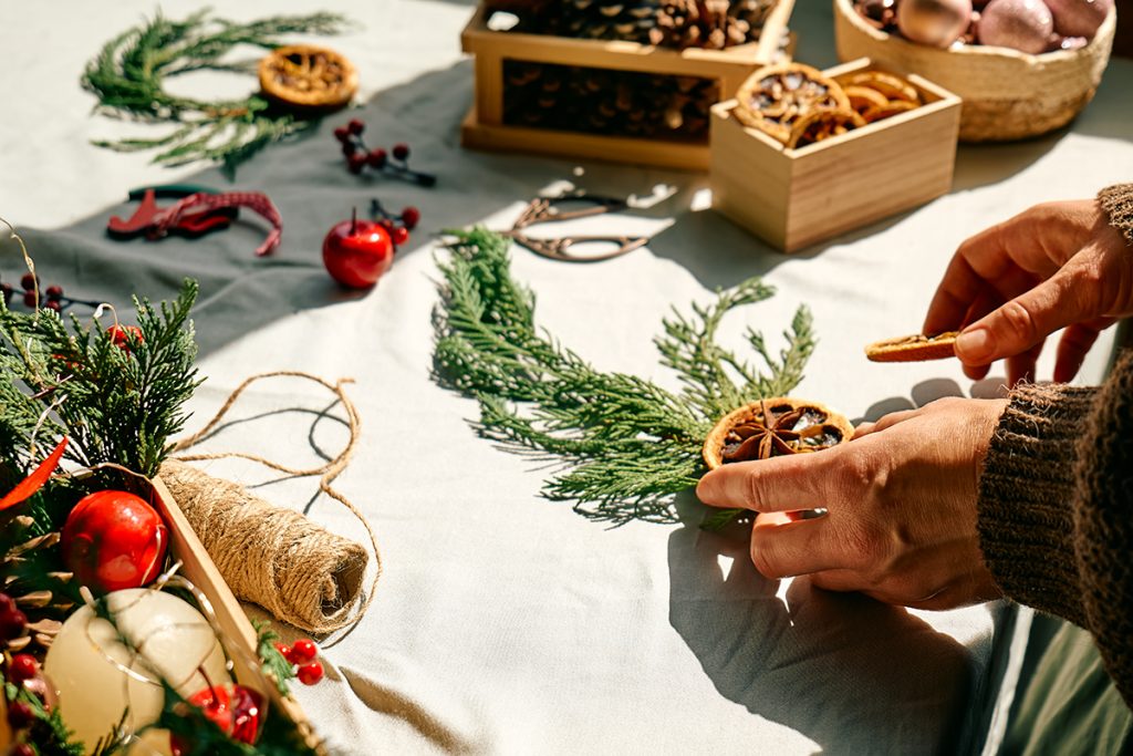 Woman making Christmas arrangement with fir branches and dried oranges. Female hands creating Christmas craft handmade decor. New year celebration. Winter holidays.