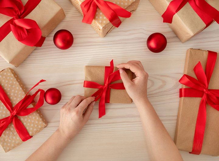 DIY hobby. Female hands wrapping christmas holiday handmade presents in paper with red ribbons. Decoration of gifts on wooden table, top view, flat lay