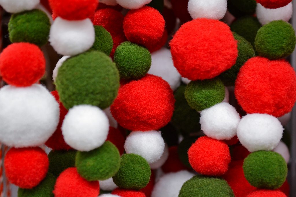 Bright garland of fluffy pompoms white, green and red as a festive background. Selective focus.