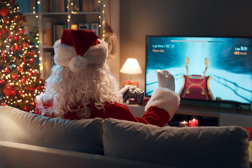 Funny Santa Claus sitting on the couch at home and playing videogames at Christmas, he is winning the game