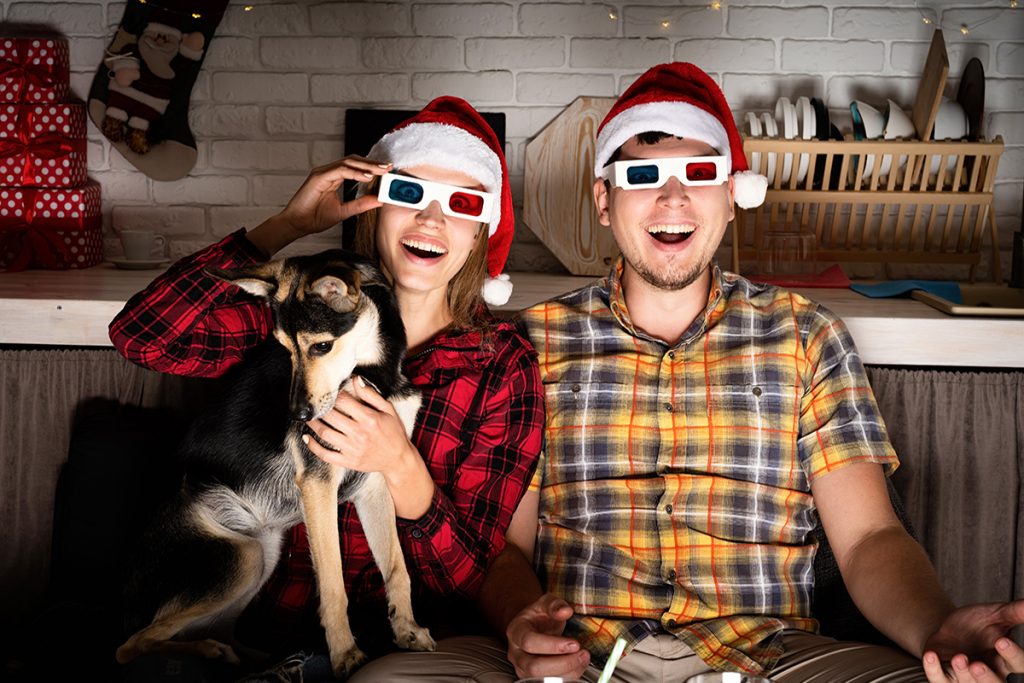 Movie night. Young couple in 3D glasses watching movies at home at christmas pointing to the screen eating popcorn